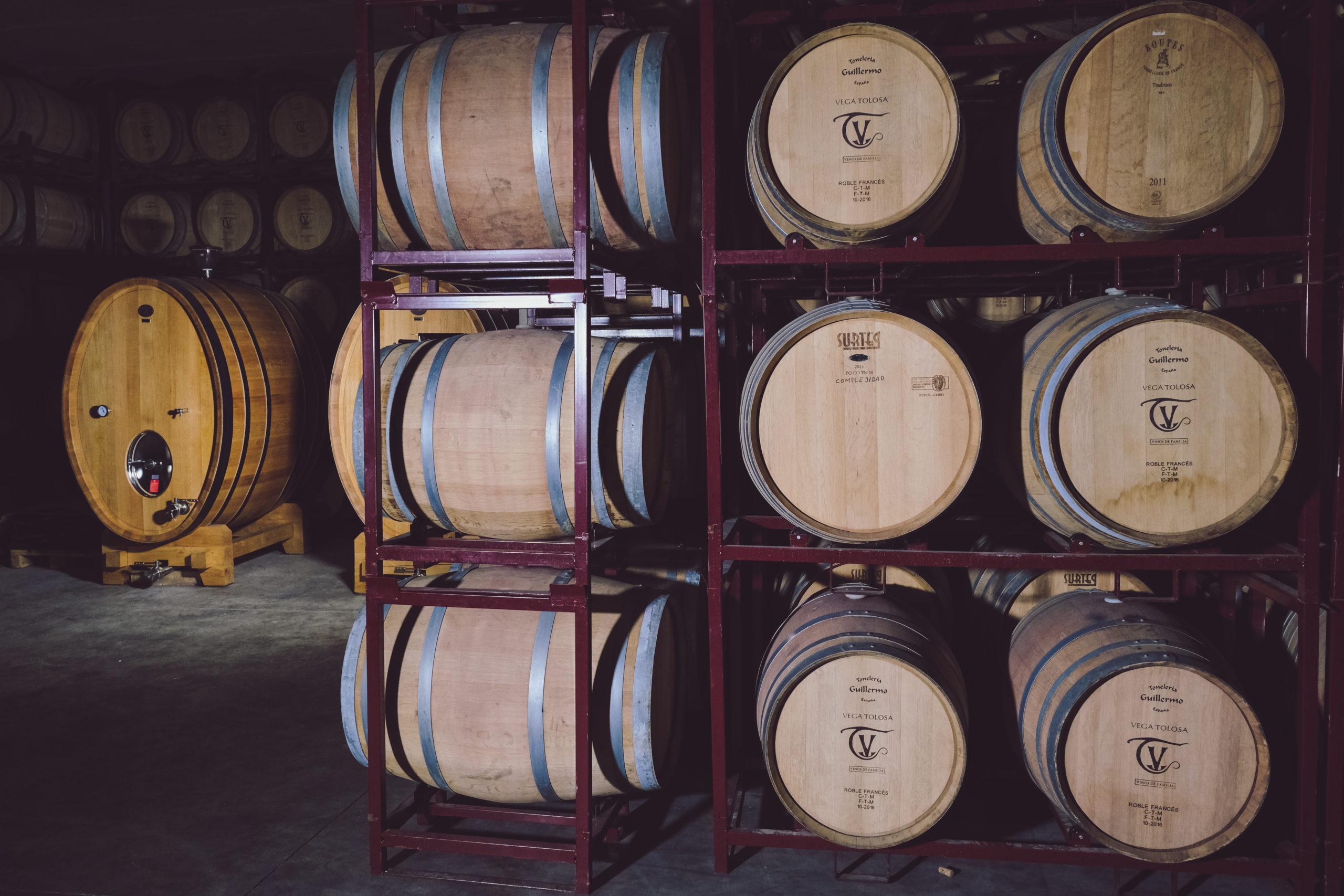Bodega de barricas de madera para vino cuidadosamente alineadas en un ambiente oscuro, ideal para los amantes del vino que desean comprar online.