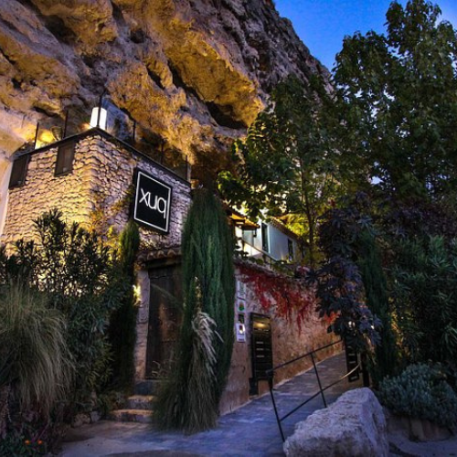 An exclusive stone building located in a mountainous landscape at dusk surrounded by lush vegetation, standing out as a limited edition accommodation experience.