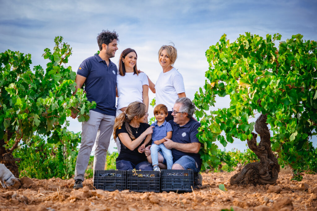 Una familia sonriente se reúne en un viñedo, rodeada de frondosas vides y cestas llenas de uvas listas para comprar online, destacando un ambiente de cultivo sostenible y la importancia del DEO en la producción vinícola.