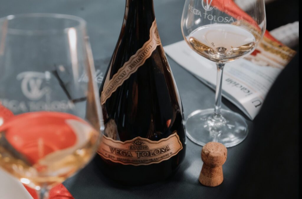 Una mesa elegante con copa y botella de vino Vega Tolosa junto a un corcho, destacando la temática de vino ecológico para una experiencia de cata sofisticada.