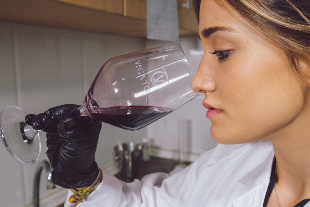 Una mujer en una sala de degustación examina atentamente vino excelente en una copa inclinada, capturando la esencia de la cata.